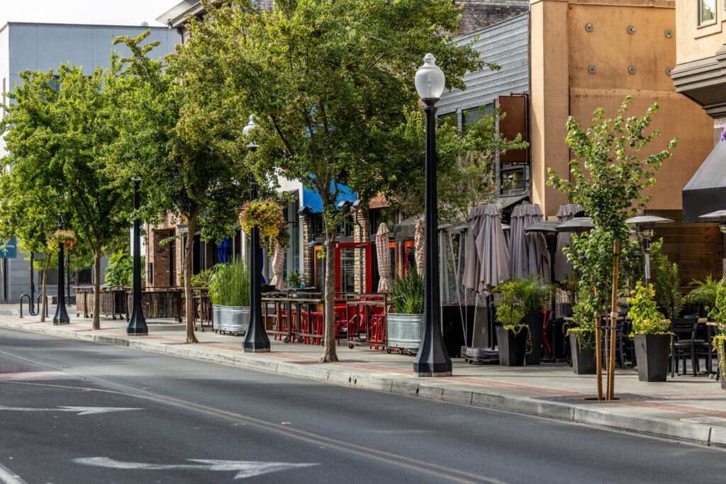 Empty street with trees and outdoor seating.