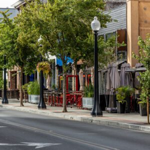 Empty street with trees and outdoor seating.