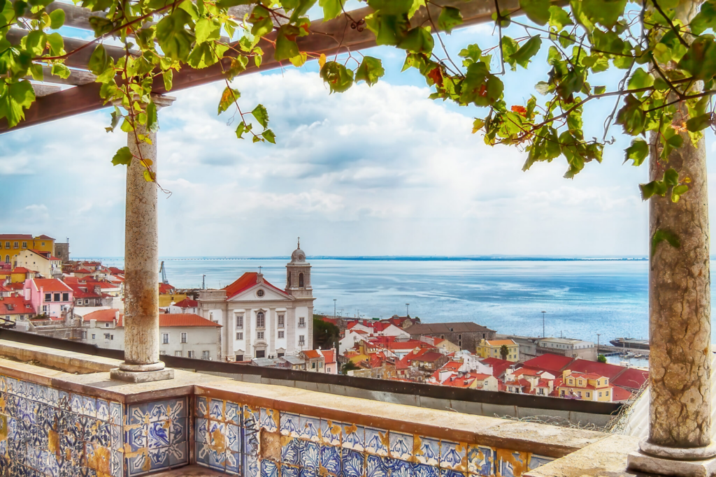 Scenic coastal town view framed by leafy branches and tiled balcony.