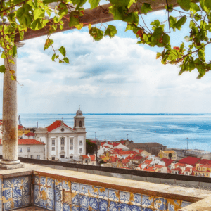 Scenic coastal town view framed by leafy branches and tiled balcony.