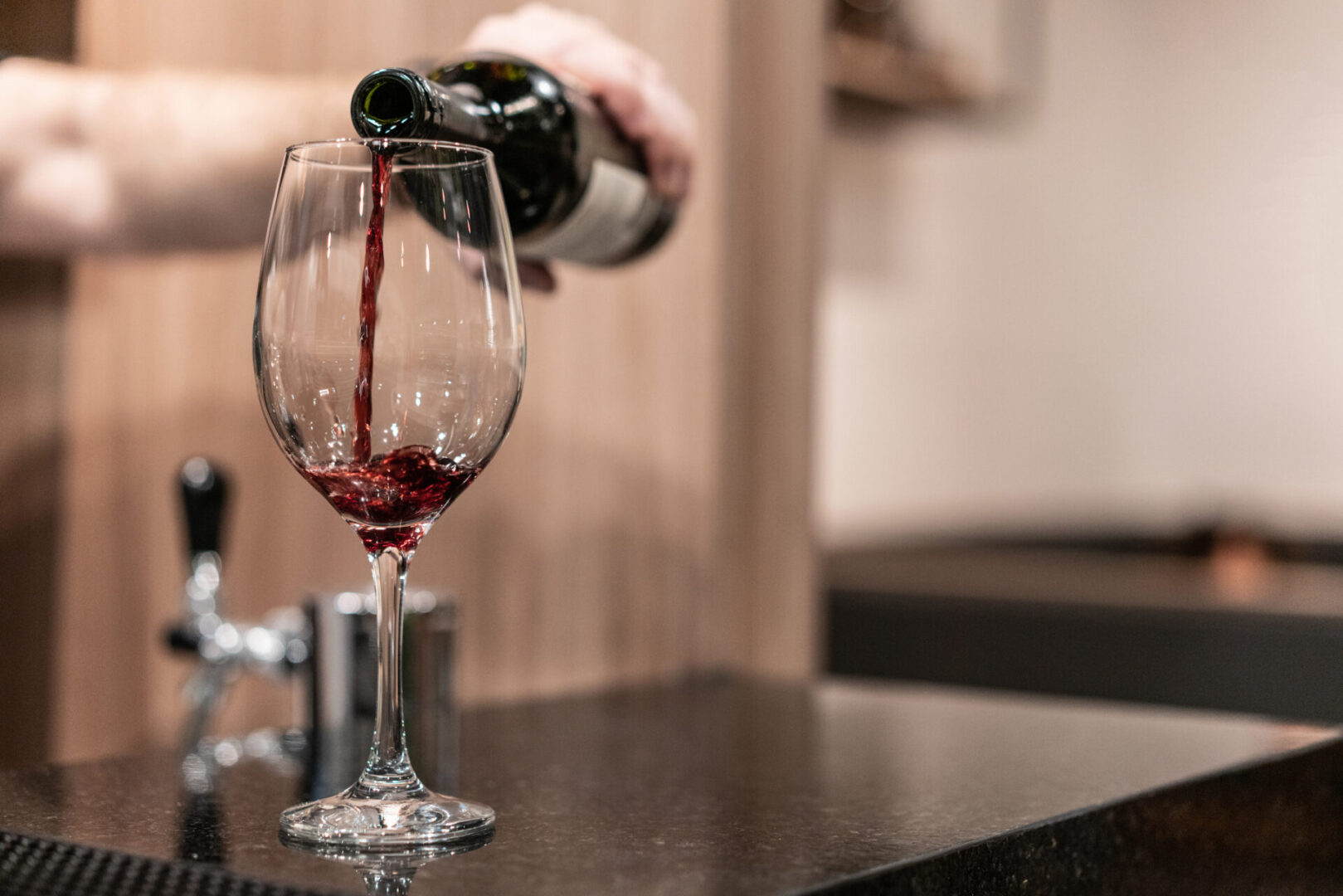 Pouring red wine into a glass at a cozy indoor setting.