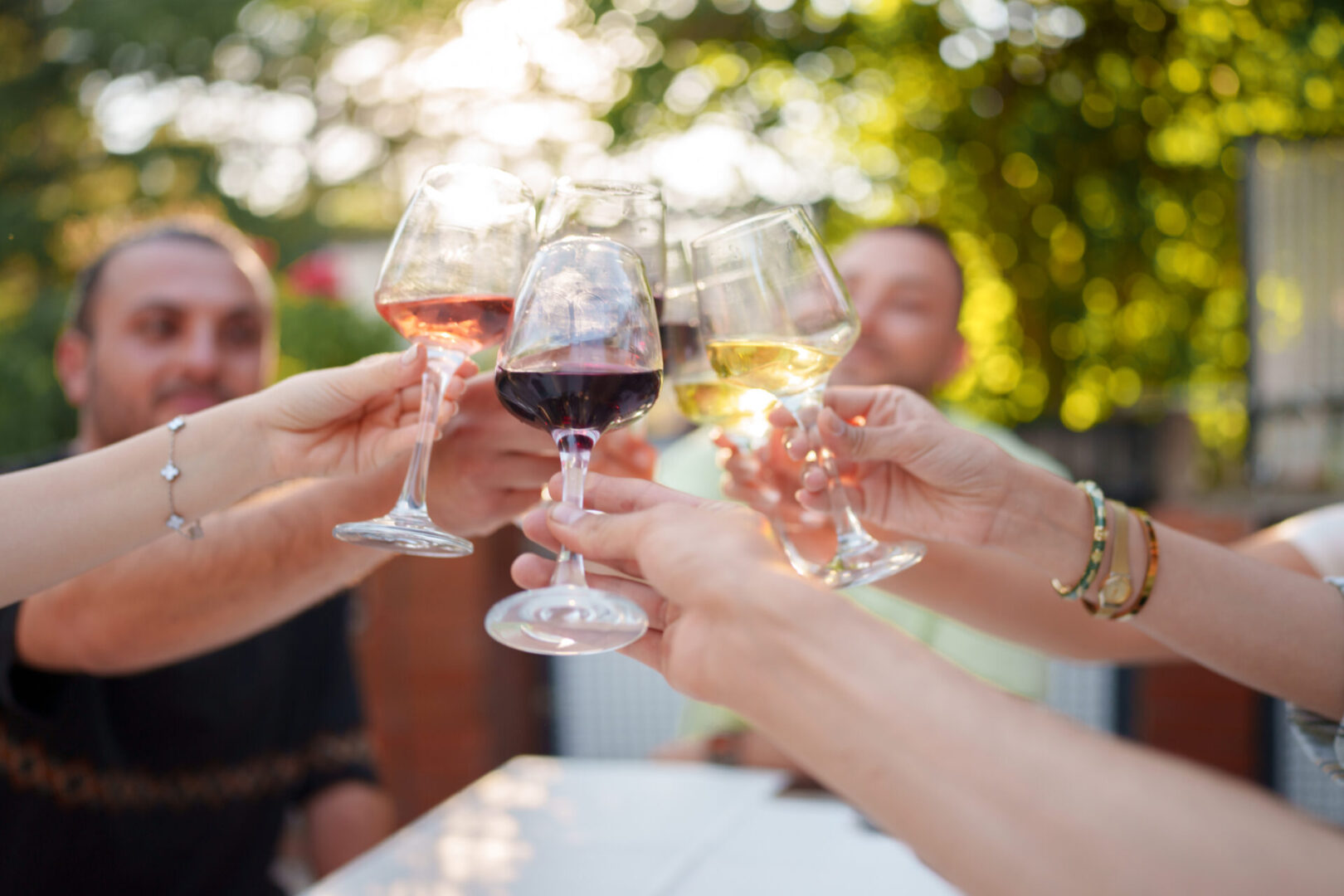 Friends clinking wine glasses outdoors in a toast.