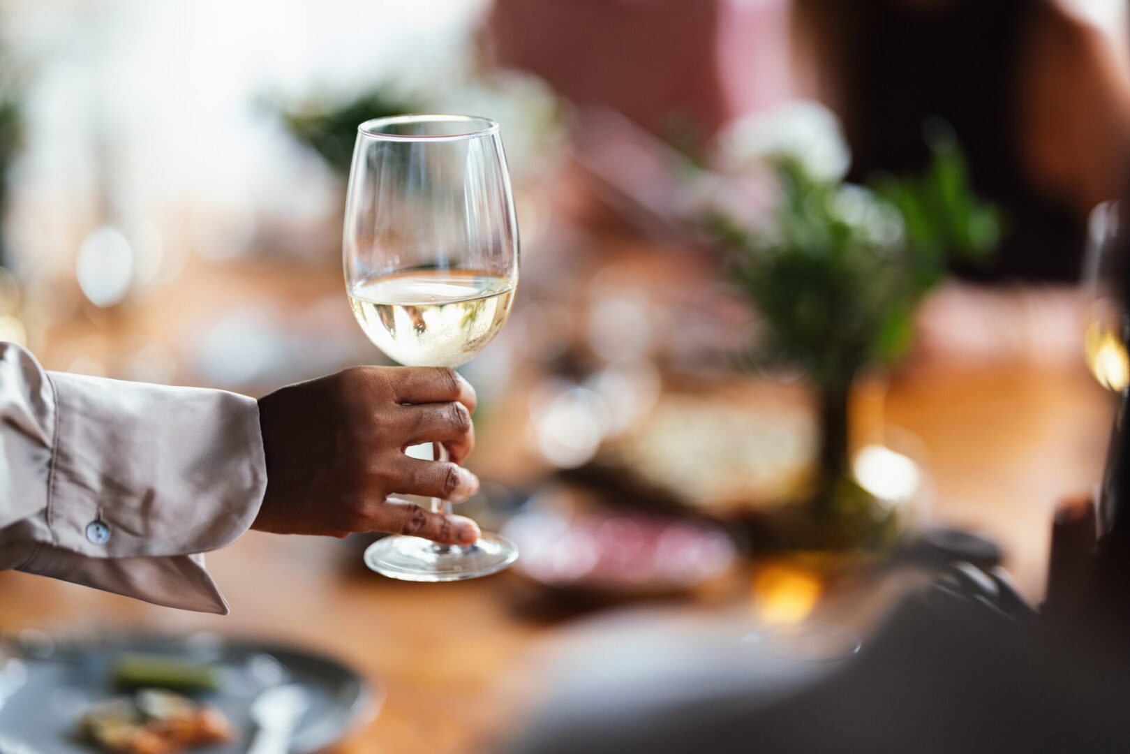 Hand holding a glass of white wine at a social gathering.