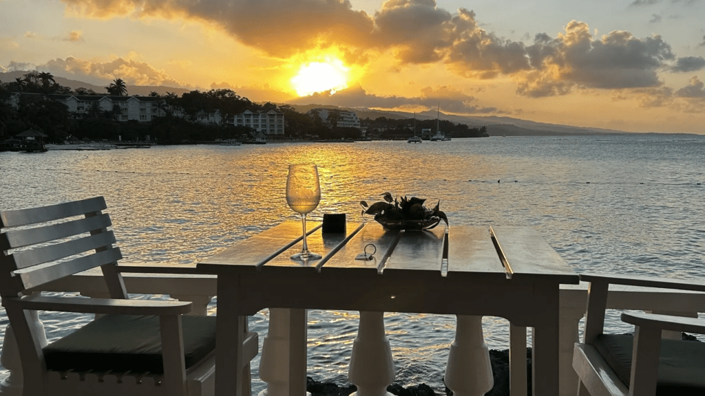 Romantic sunset dinner setup by the water with wine glasses and flowers.