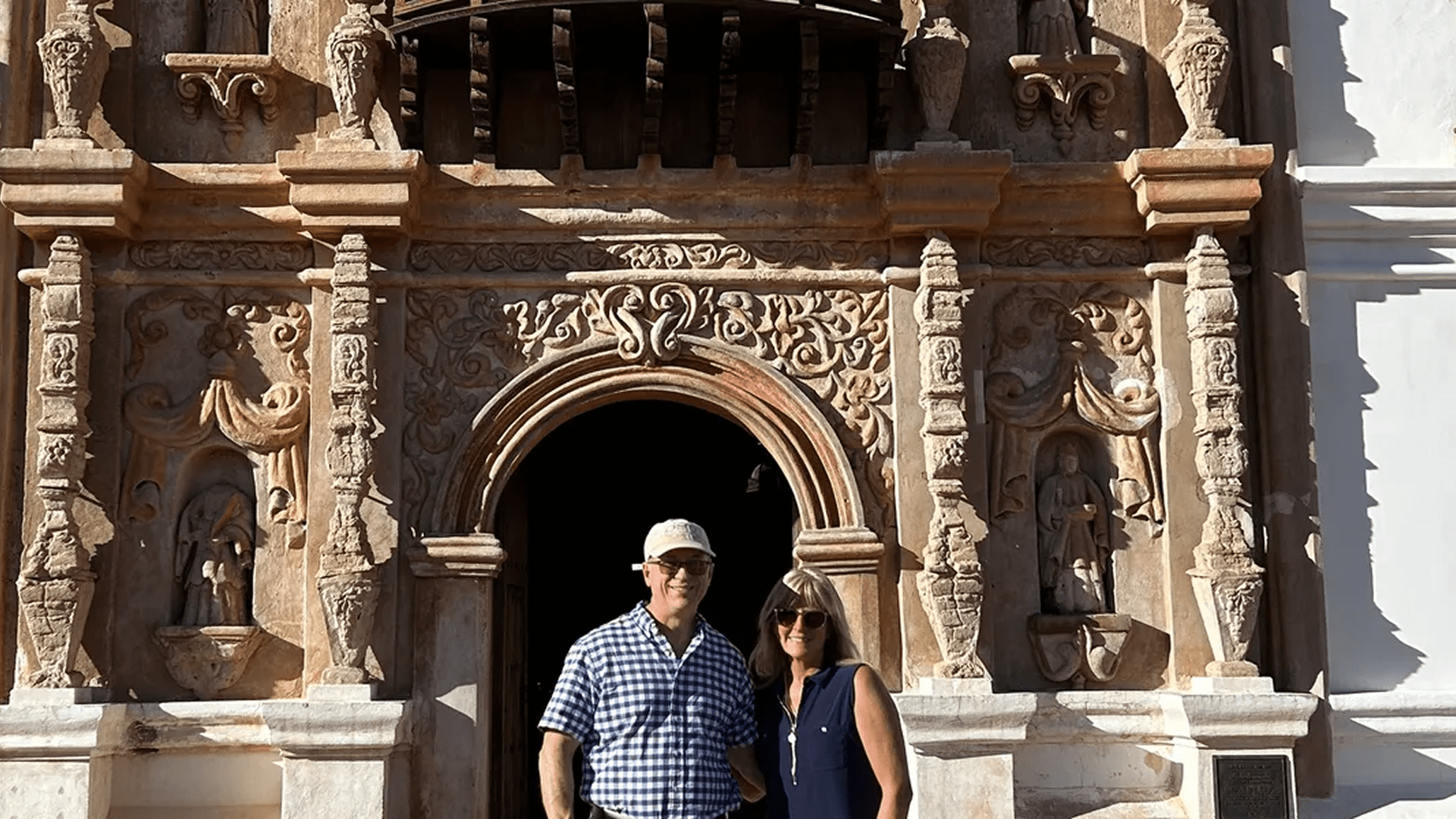 A couple poses in front of an ornate historic stone archway.