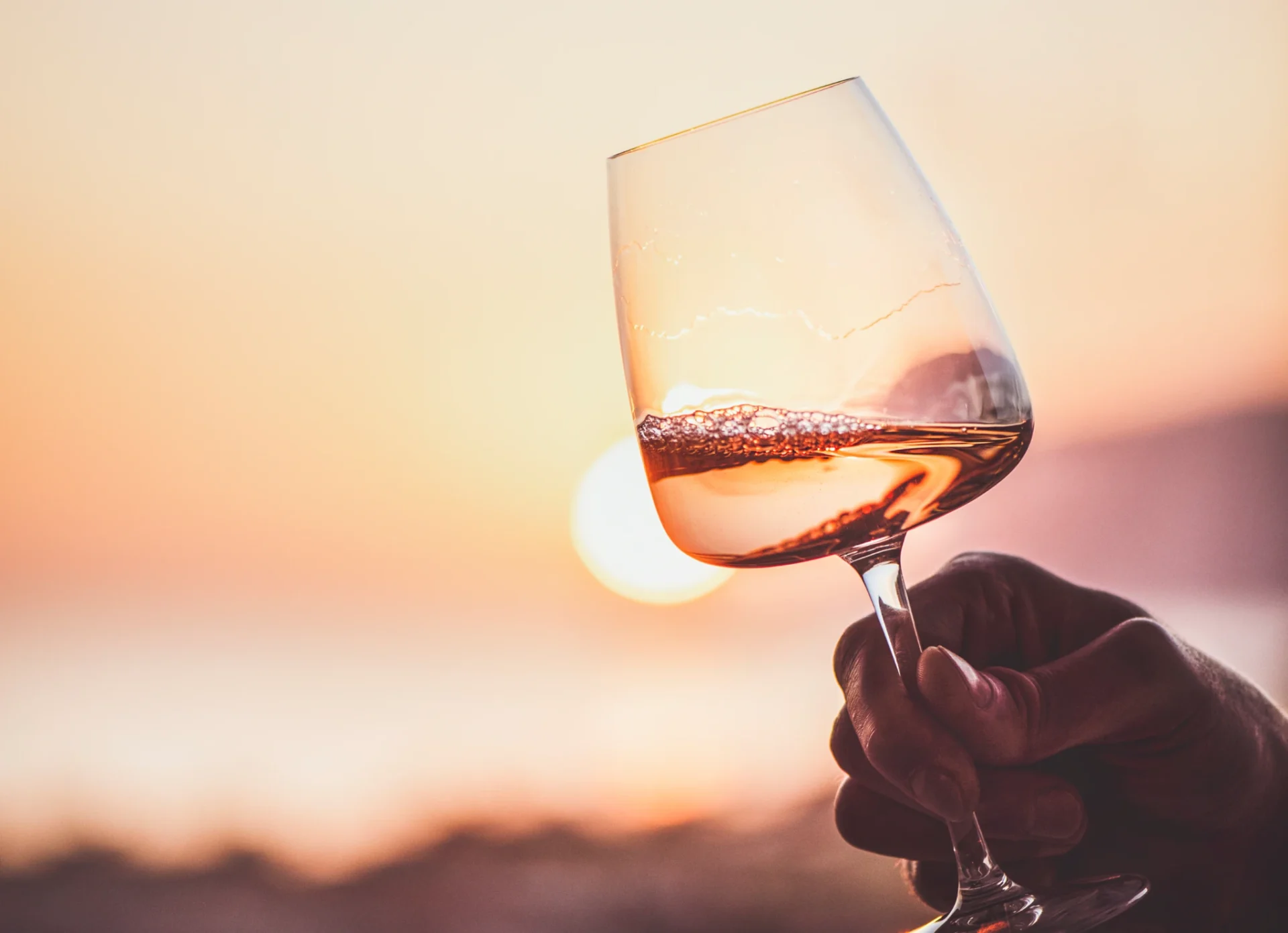 Hand holding a wine glass against a sunset.