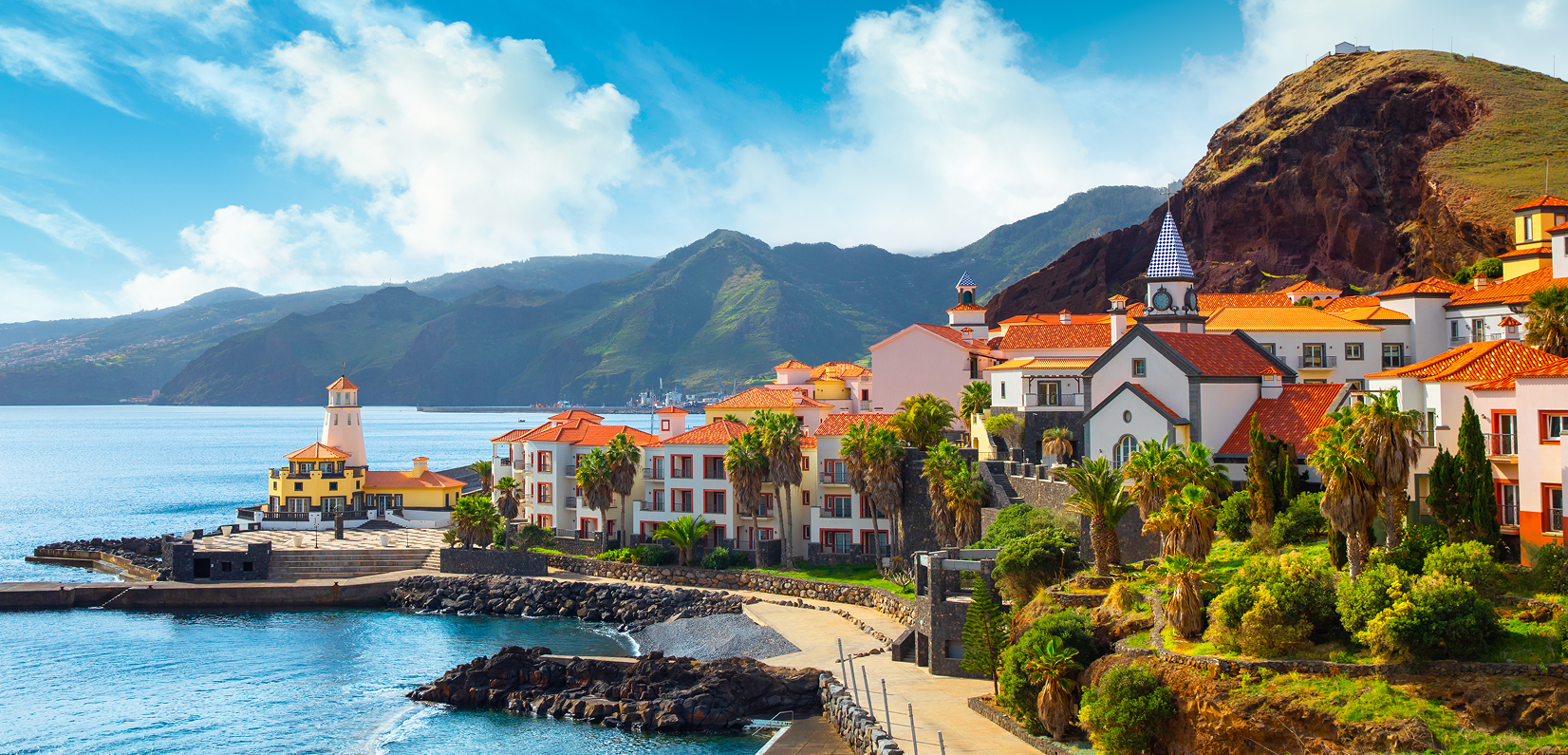 Coastal town with colorful buildings and mountains under a blue sky.