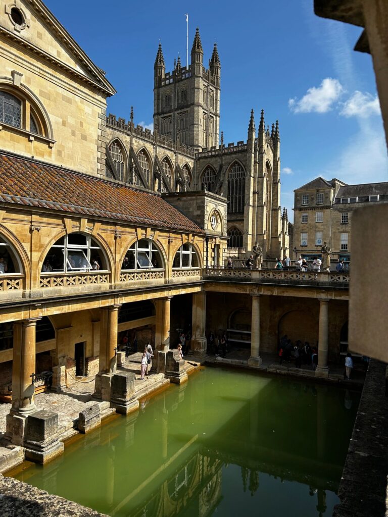 Historic Roman-style bath with ancient architecture and green water under a blue sky.