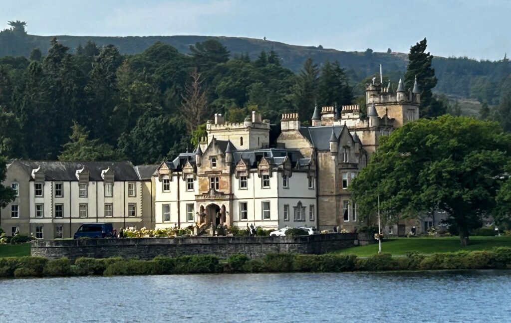 A grand castle by a lake with forested hills in the background.