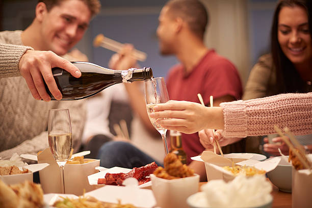 Friends pouring champagne over shared takeout dinner