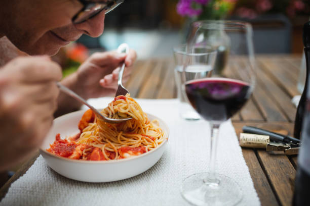 Person twirling spaghetti beside red wine